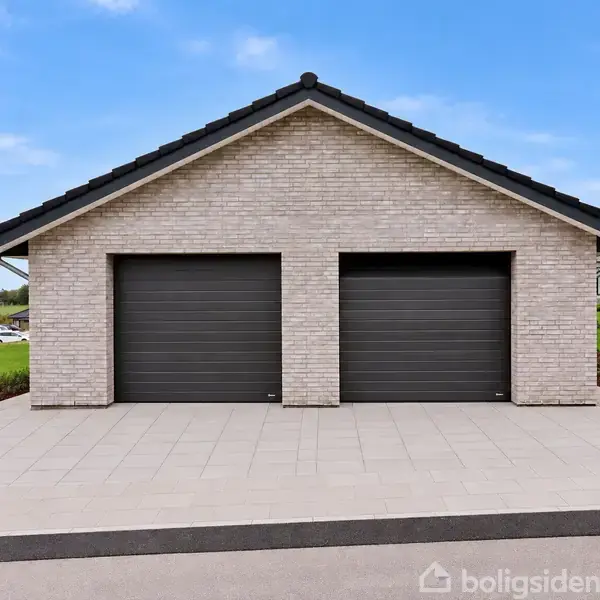 To sorte garageporte i en lys stenbygning står lukkede, placeret i en velplejet have med græsplæner og ved et åbent, landligt område under en klar blå himmel.