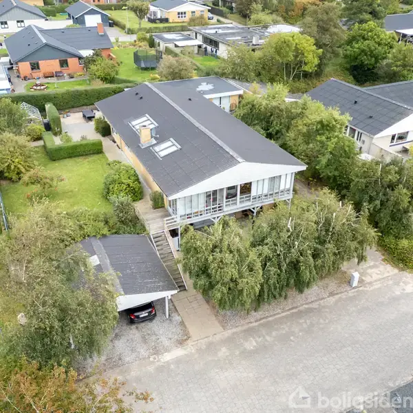 Et moderne to-etagers hus ligger i et grønt parcelhuskvarter. Huset har en stor glasveranda og sort tag. Omgivet af en velplejet have og flere træer.