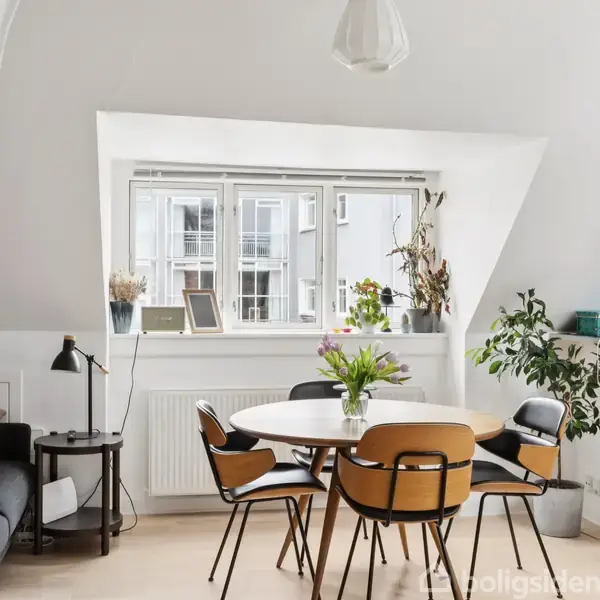 Et rundt spisebord med stole står foran et stort, solbelyst vindue, omgivet af grønne planter og indretningsgenstande i en lys lejlighed.