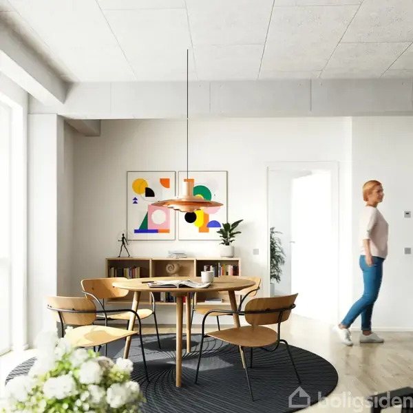 En rund spisebordsgruppe står i midten af et lyst rum. En kvinde går forbi i baggrunden; moderne kunst hænger på væggen og en plante står ved reolen.