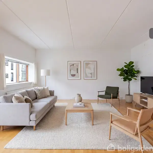 Stue med grå sofa, træstol og moderne tv-skænk. Sofaen har puder, og sofabordet er dekoreret med bøger. Store vinduer og to billedrammer på væggen. Tekst: "Visualisering".