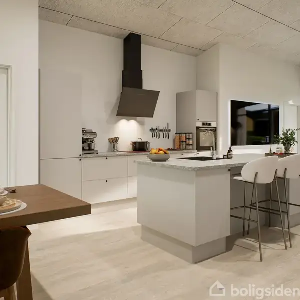 Køkken med hvidt køkkenbord omkranset af barstole, hvor køkkenudstyr og frugt er placeret. Moderne interiør med spisebord til venstre og stor vinduesåbning mod haven til højre.
