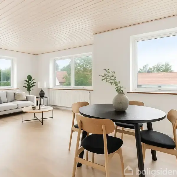 En lys stue indeholder en beige sofa med puder, sofabord med en plante, spisestue med fire stole og kunst på væggen, træloft og store vinduer udsigt til huse og træer.