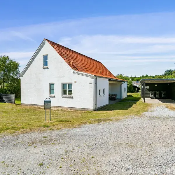 Hus med hvid facade og rødt tag står i en have med græsplæne. Til højre ses en carport, omgivet af træer i baggrunden. Ingen tekst findes i billedet.
