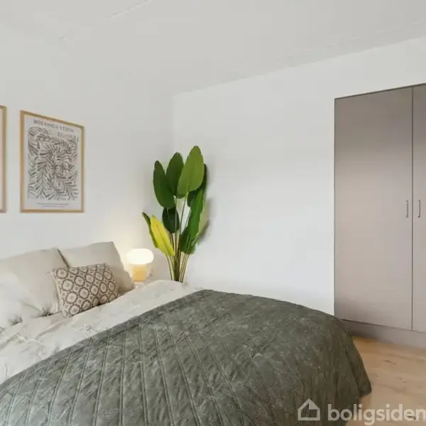 Soveværelse med seng dækket af grønt sengetæppe, pyntepuder og kunstværker på væggen. En stor plante står ved siden af sengen, som er tændt af en lampe, ved siden af et skab. Tekst: "PICASSO", "MÚSÉE DE RENNES".