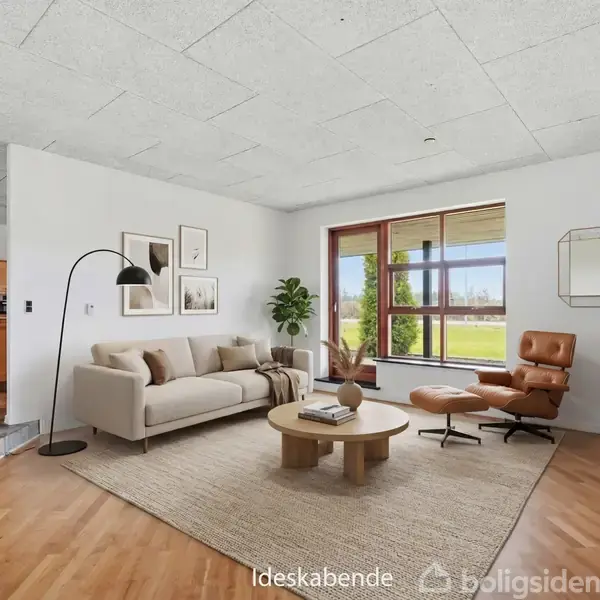 En moderne stue har en beige sofa og en lænestol nær et stort vindue, der lukker lys ind. Et rundt sofabord og planter pryder rummet. Tekst: "Ideskabende".