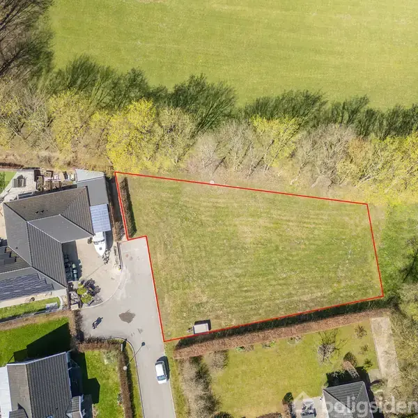 Grunden er markeret med en rød linje og ligger ved siden af en moderne bolig med grå tag. Omgivet af træer og grønne områder, ses også en parkeret bil.