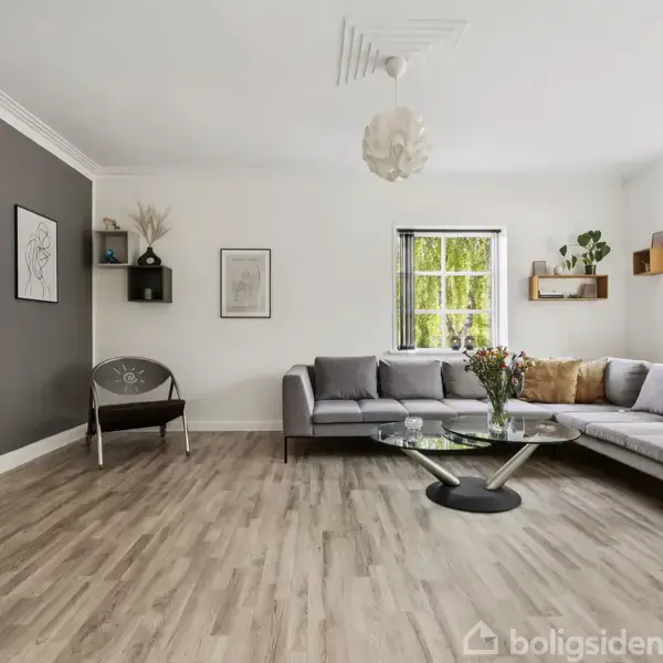 Stue med grå hjørnesofa og rundt, sort sofabord; store vinduer giver lys; vægge dekoreret med hylder og billeder; trægulv; moderne og minimalistisk indretning.
