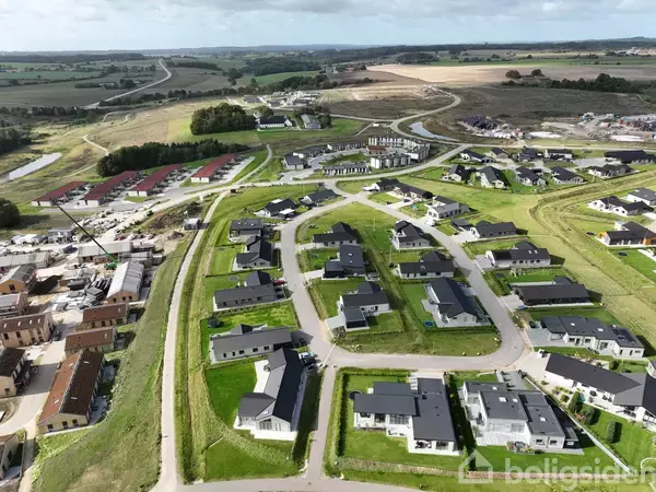 Boligområde med moderne huse i rækkeformation ligger i et grønt landskab. Til venstre ses et område under opførelse. I baggrunden breder marker og veje sig ud.