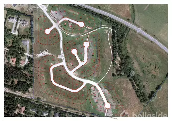 Luftfoto af et byggegrundsområde med hvide veje i et forgrenet mønster omgivet af grønne marker. Der er spredte boliger og en vej i nærheden.