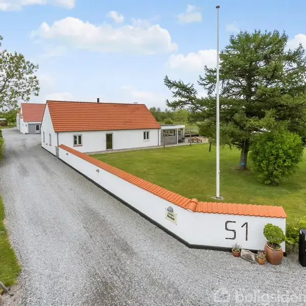 Hvidt hus med rødt tag står stillestående, omgivet af en grusvej og grønne græsplæner. Nummer 51 er malet på en hvid mur ved indkørslen.