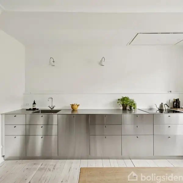 Et moderne køkken med stålskabe og hvid væg dekoreret med to væglamper. Bordet har køkkenredskaber og en plante. Trægulv danner en lys og minimalistisk atmosfære.