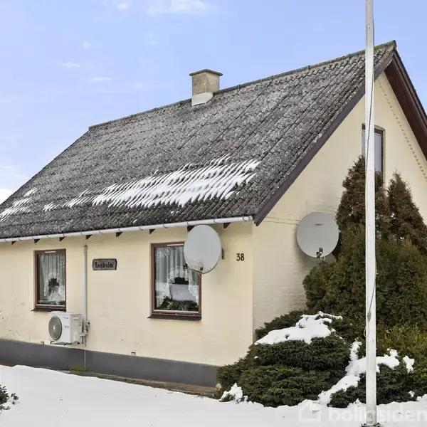 Hus med sadeltag har sne på taget og satellitantenner på ydervæggen; omgivet af snebeklædt have. Husnummeret 38 er synligt.