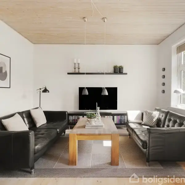 To sorte lædersofaer står omkring et træbord i en stue. Vægdekorationer, planter og lamper skaber en hyggelig atmosfære. Store vinduer lader lys strømme ind i rummet.