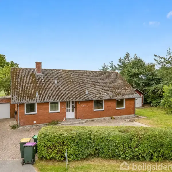Et rødt bondehus med gråtag ligger stille omgivet af grønne marker og træer. Et lille udhus står ved siden af huset. Landskabet strækker sig til horisonten.