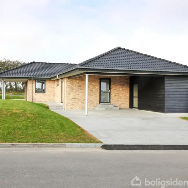 En moderne enfamilieshus står på en nyslået græsplæne. Huset har rød murstensfacade, sort tegltag og en indkørsel i beton. Det er omgivet af åbne grønne områder.