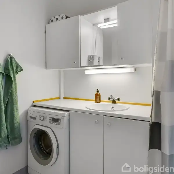 Stue med lædersofaer omkring et sofabord. Fjernsyn står mod en skråvæg. Spisebord med stole i baggrunden. Lysindfald fra ovenlys. Væggene har indrammede billeder.