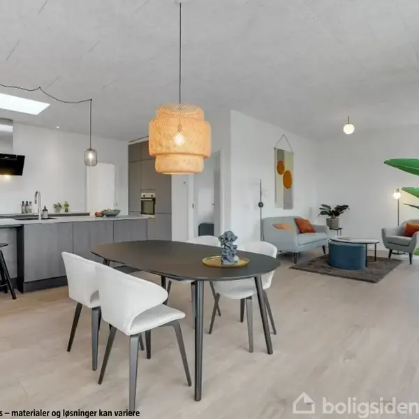 Et moderne køkken-alrum har et ovalt spisebord med stole, en stor grøn plante og en sofagruppe i baggrunden. Tekst: "Visualisering af udstillingshus – materialer og løsninger kan variere".