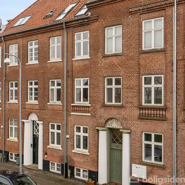 Bygning i mursten med flere etager og klassiske vinduer. Indgangene er dekoreret og et gadelys står tæt ved. Det ser ud til at være en bykontekst.