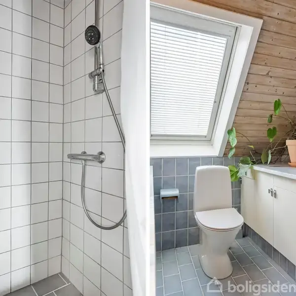 Bruser med hvid flisebelægning står i et badeværelse ved siden af et toilet. Vindue med skrå væg, hvid skabselement og potteplante fuldender rummet.
