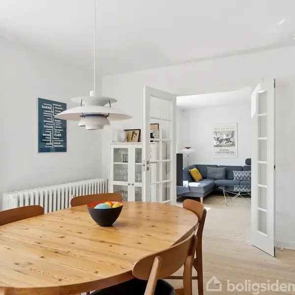 Brusekabine med hvide fliser. Vaskemaskine står til venstre. En håndvask er placeret ved vinduet. Der er planter på hylden og gulvet. Toiletrulleholder ses ved siden af vasken.