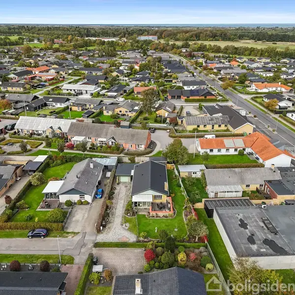 Et boligkvarter set fra luften, med huse der er omgivet af grønne haver og veje. Området er tæt bebygget med flere huse af forskellig størrelse.