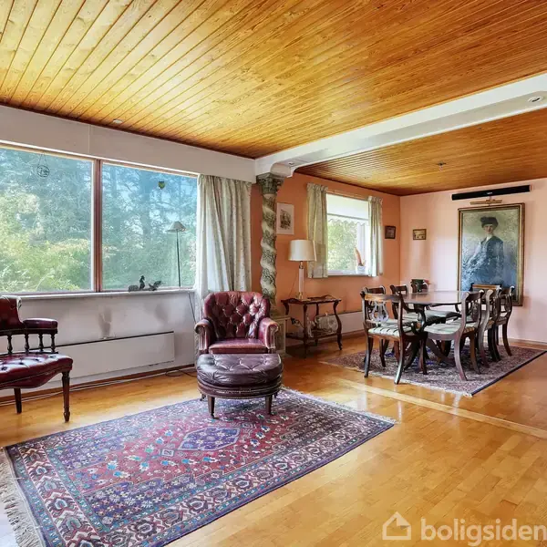 Stue med træloft, der har et siddeområde med røde lænestole og et spisebord. Store vinduer til venstre giver udsigt til træer. Babysæde på gulvet.