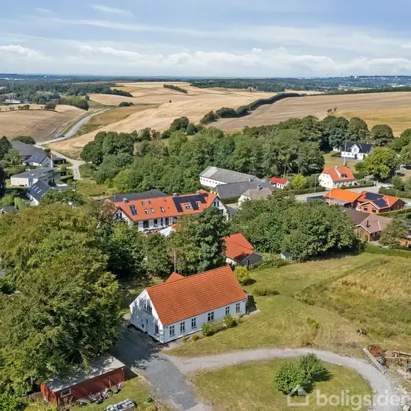 Røde tage pryder huse i en landsby, der omgives af frodige marker og skovområder. Veje snor sig gennem området, der er indhyllet i en landlig atmosfære fyldt med grøn natur.