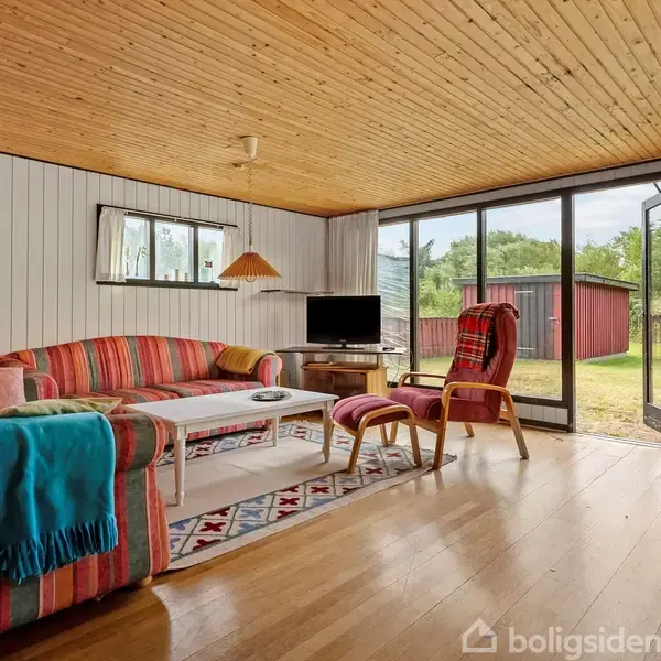 Farverig sofa med tæppe og puder står ved et sofabord på et tæppe. En lænestol ved en glasvæg åbner ud mod en have med et rødt skur.