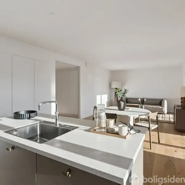 Køkkenø med vask og serveringsbakke står centralt. I baggrunden ses en lys stue med sofa, sofabord og dekorative planter. Sollys strømmer ind i det moderne, minimalistiske rum.