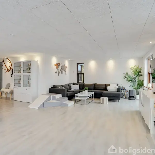 Stue med sort sofa i hjørne, dekoreret med verdenskort på væggen, en plante ved siden af fjernsynet. Legetøjsbiler er placeret oven på skabet, og rensdyrgevirer hænger på væggen.