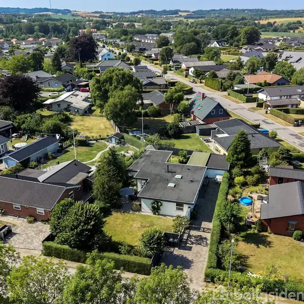 Boligområde set fra oven viser huse med haver i en landsby. Grusveje adskiller de velholdte ejendomme. I baggrunden ses åbne marker og skovklædte områder.