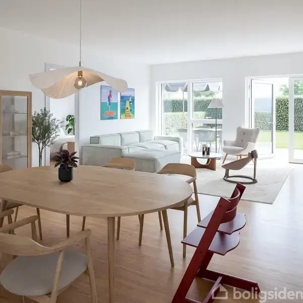 Rundt træbord med stole står i en stue med lys indretning; sofa og lænestol nær store vinduer, planter og kunst på væggen, trægulv og døre åbner til en have.