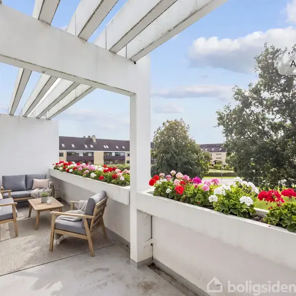 En altan med træmøbler og planter i blomsterkasser. To stole og en sofa står omkring et lille bord. Baggrunden viser træer og en boligblok. Tekst: "AI visualisering".