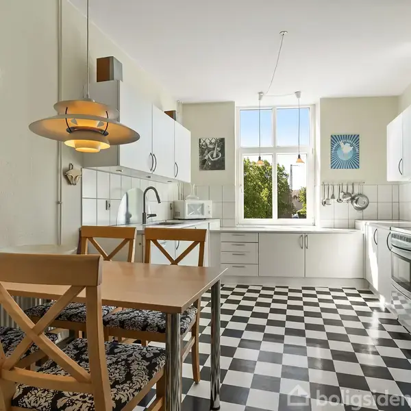 Køkken med sort-hvid ternet gulv, spisebord og fire træstole. En lampe hænger over bordet. Køkkenskabe, vask og ovn langs væggene. Vægur viser kl. 10:10. Grøn udsigt gennem vindue.