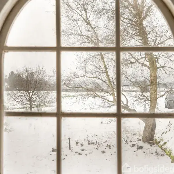 Bueformet vindue med udsigt til sneklædt landskab; træer står stille i den vinterlige scene udenfor.