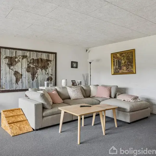 Grå hjørnesofa med lyse puder står i stue med gråt gulvtæppe. Et træbord står foran sofaen, og verdenskortkunst hænger på væggen bagved.