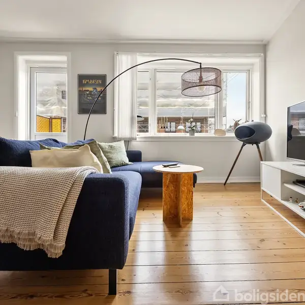 En mørkeblå sofa står i en lysestue med fyrretræsgulve. En buet lampe hænger over et lille rundt træbord. Et TV placeret på et hvidt TV-bord.