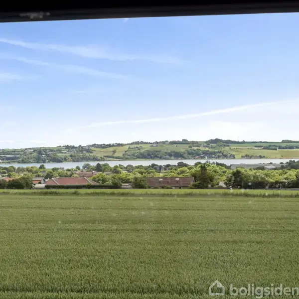 Udsigt over en grøn mark set fra et vindue. Fjern baggrund viser bakker og en flod under en klar blå himmel.
