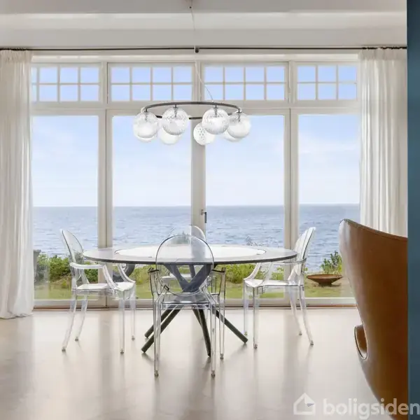 Stråtækt hus beliggende på en græsbeklædt bakketop med udsigt over havet; omgivet af frodig skov.