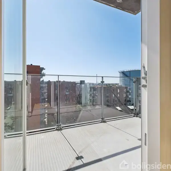 Terrassen er omgivet af glasrækværk og åbne døre, med udsyn til byens tage og bygninger i baggrunden. Sollys fylder scenen med en klar, blå himmel.