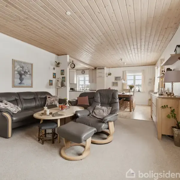 Lædersofa og lænestol med fodskammel står i stue, oplyst af dagslys fra vinduer. Rundt sofabord med dekorative genstande. Træloft og lyse vægge bidrager til en hyggelig atmosfære.