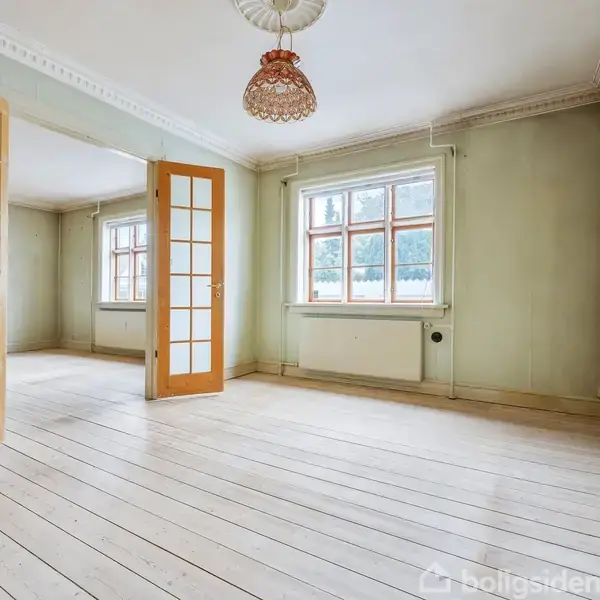 Et tomt rum med lyse trægulve og hvide vægge. To glasdøre står åbne mellem rummene. Store vinduer slipper naturligt lys ind. En simpel lampe hænger fra loftet.