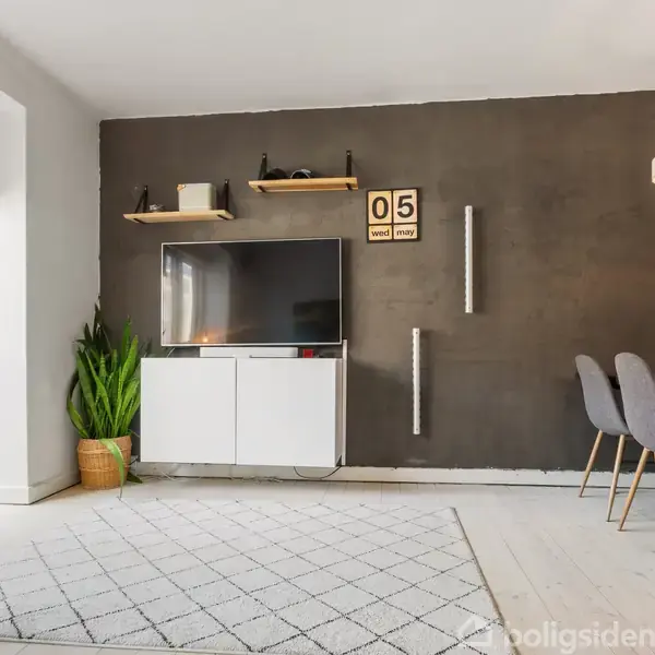 Et moderne stueinteriør viser en fladskærms-TV på en hvid skænk mod en mørk væg. Ved siden af står en plante, og en spisebordssæt med stole ses til højre.