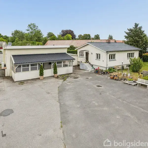Et hvidt træhus med flere vinduer står i en grøn have med græsplæne. Bygningen har en betonsokkel og ses fra siden i et åbent udendørsområde.