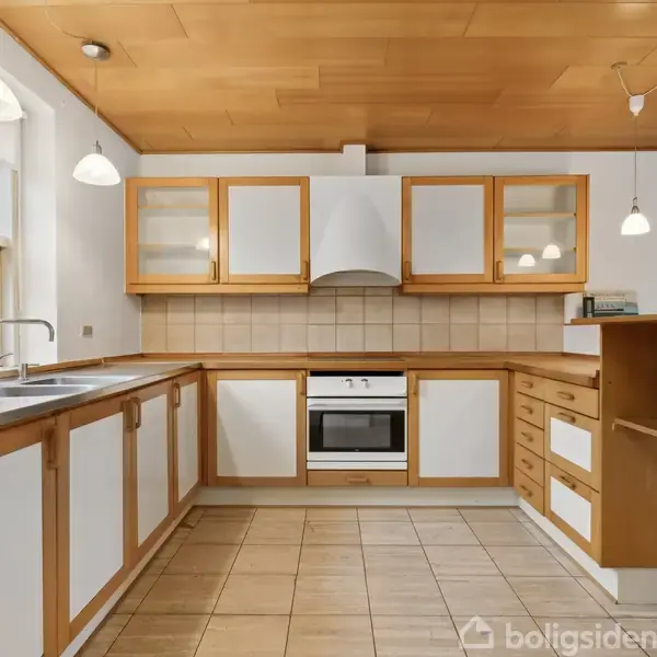 Køkken med hvide skabe og trækanter. Indbygningsovn under emhætte. Bordplader med integreret håndvask. Flere hængende lamper. Flisegulv. Stor vindue til venstre giver udsigt til have.