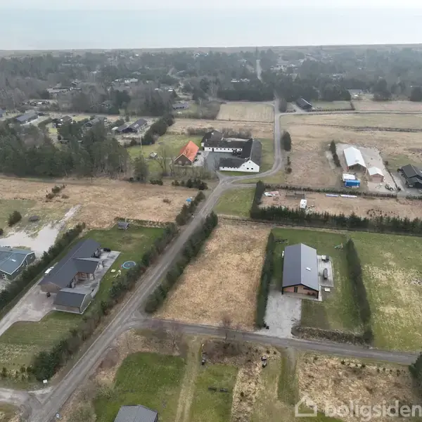 Luftfoto af et landligt område viser huse og gårde spredt mellem marker og veje. Omkringliggende natur dominerer med træer og grønne arealer, mens strukturer står langs vejene.