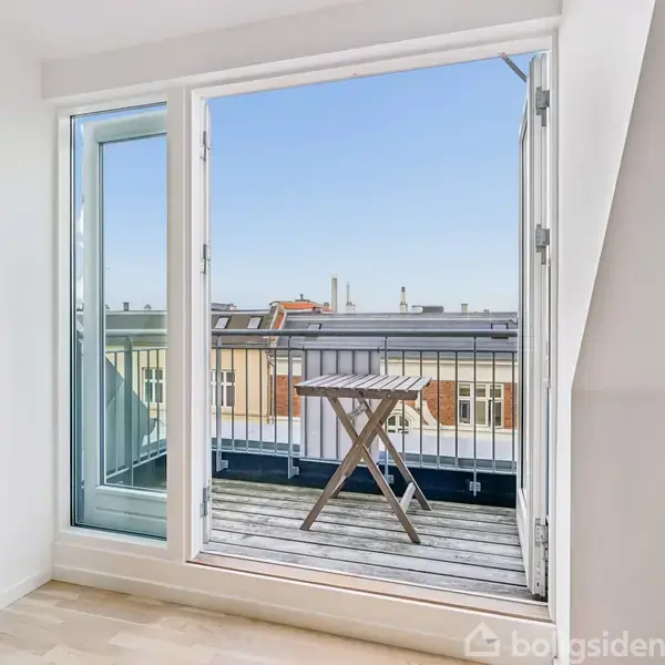Lille, sammenklappeligt bord står på en altan. Altandøren er åben fra et lyst rum med trægulv. Udsigt til blå himmel og hustage i baggrunden.