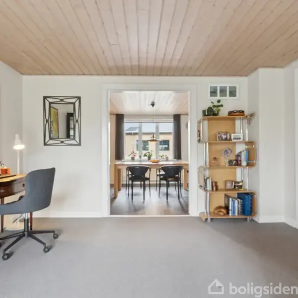 Et badeværelse med en moderne brusekabine, der har brune fliser og et guldbruserhoved. En hvid vask med en grå dispenser og et spejl hænger på væggen. Skiltning: "boligsiden".