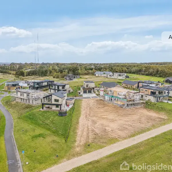 Nye huse bygges på græsareal i et boligområde. Flere moderne bygninger står langs en vej, omgivet af grønne marker og skov i baggrunden. Tekst: "AI visualisering".
